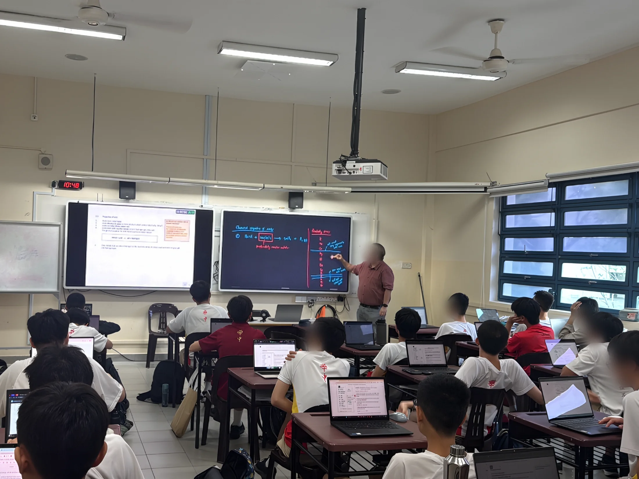 A lesson at Hwa Chong Institution: students with laptops face two ClassIn Boards while the teacher writes on one.