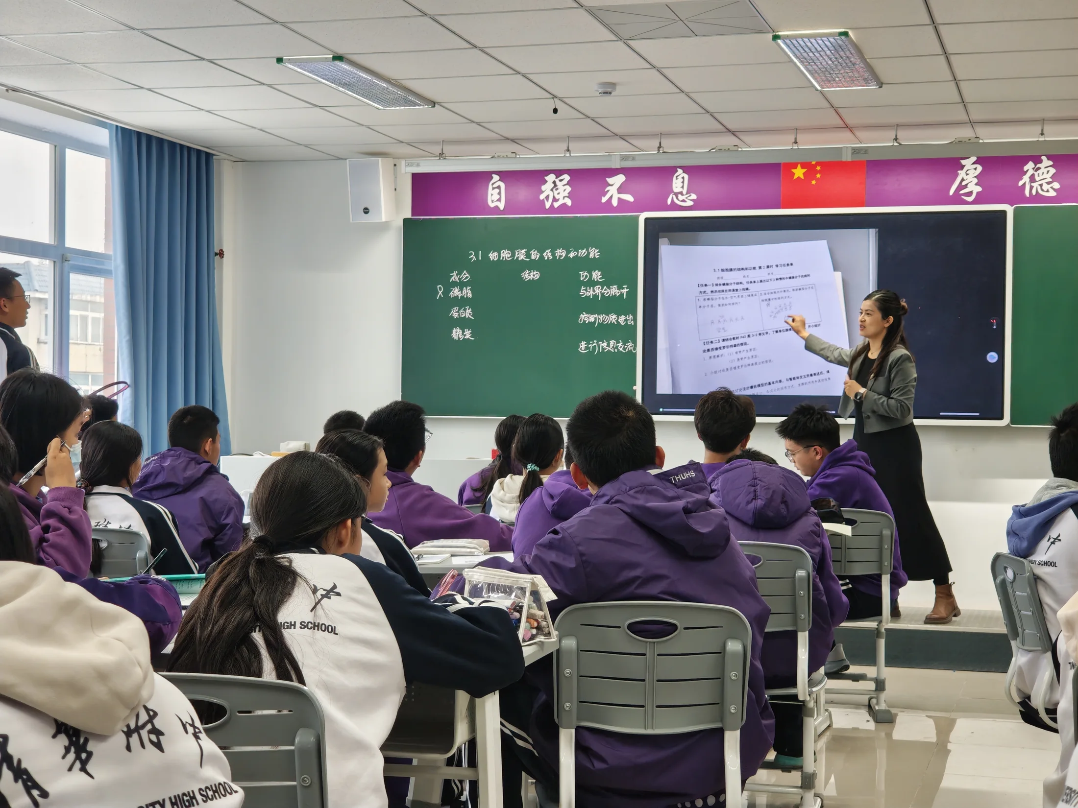 A lesson at Tsinghua University High School: the teacher works at a ClassIn screen between two chalkboards while students in school jackets follow.